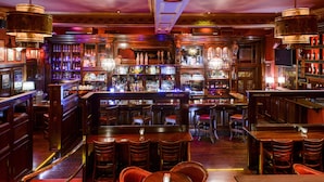 Een bar met houten meubels, barstoelen en flessen op de planken.