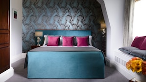 Een slaapkamer met een groot bed, behang met een patroon, een nachtkastje met een lamp en een raam met gordijnen.
