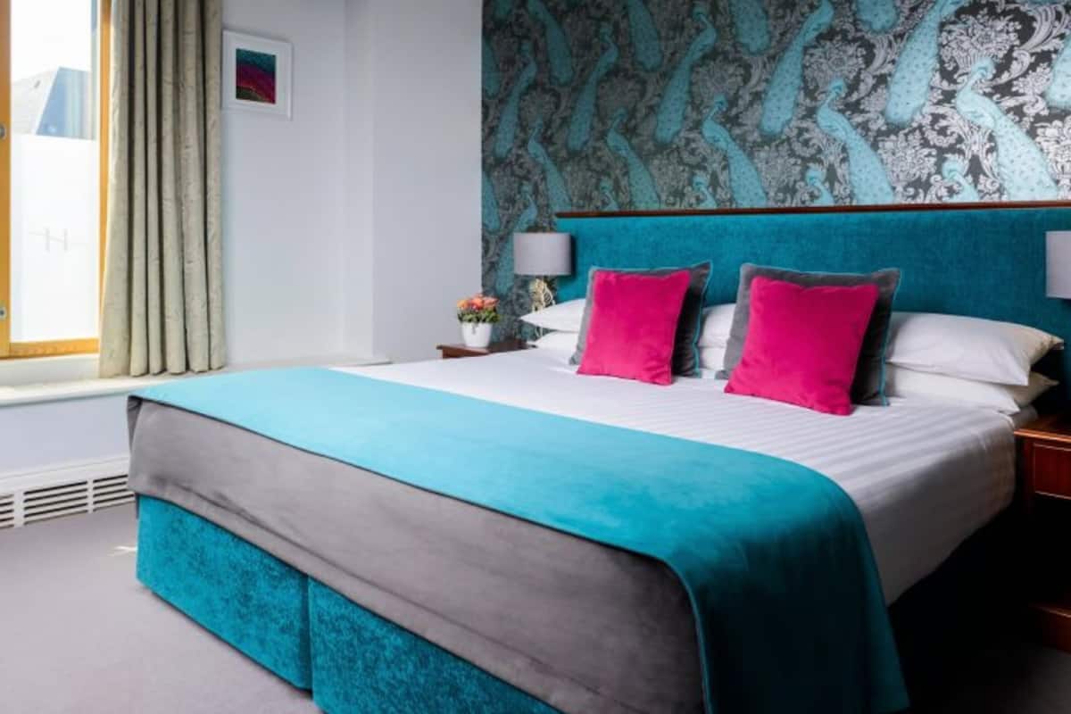 Ein Schlafzimmer mit einem Bett, Vorhängen, einem Nachttisch, einer Lampe und einer Wand mit einem gemusterten Design.