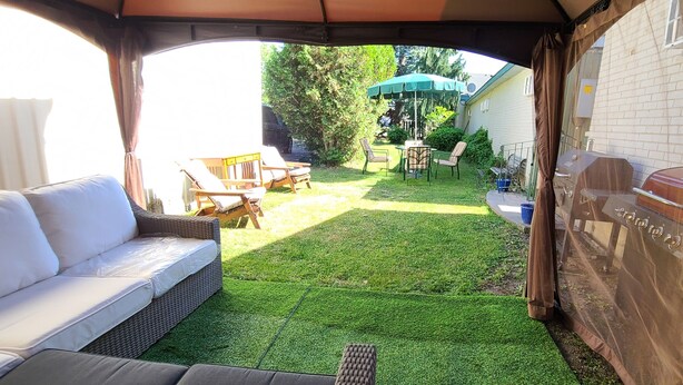 A covered outdoor seating area with a white sofa, a dining table with chairs, and a barbecue grill. - Maple Leaf Motel (Goderich)
