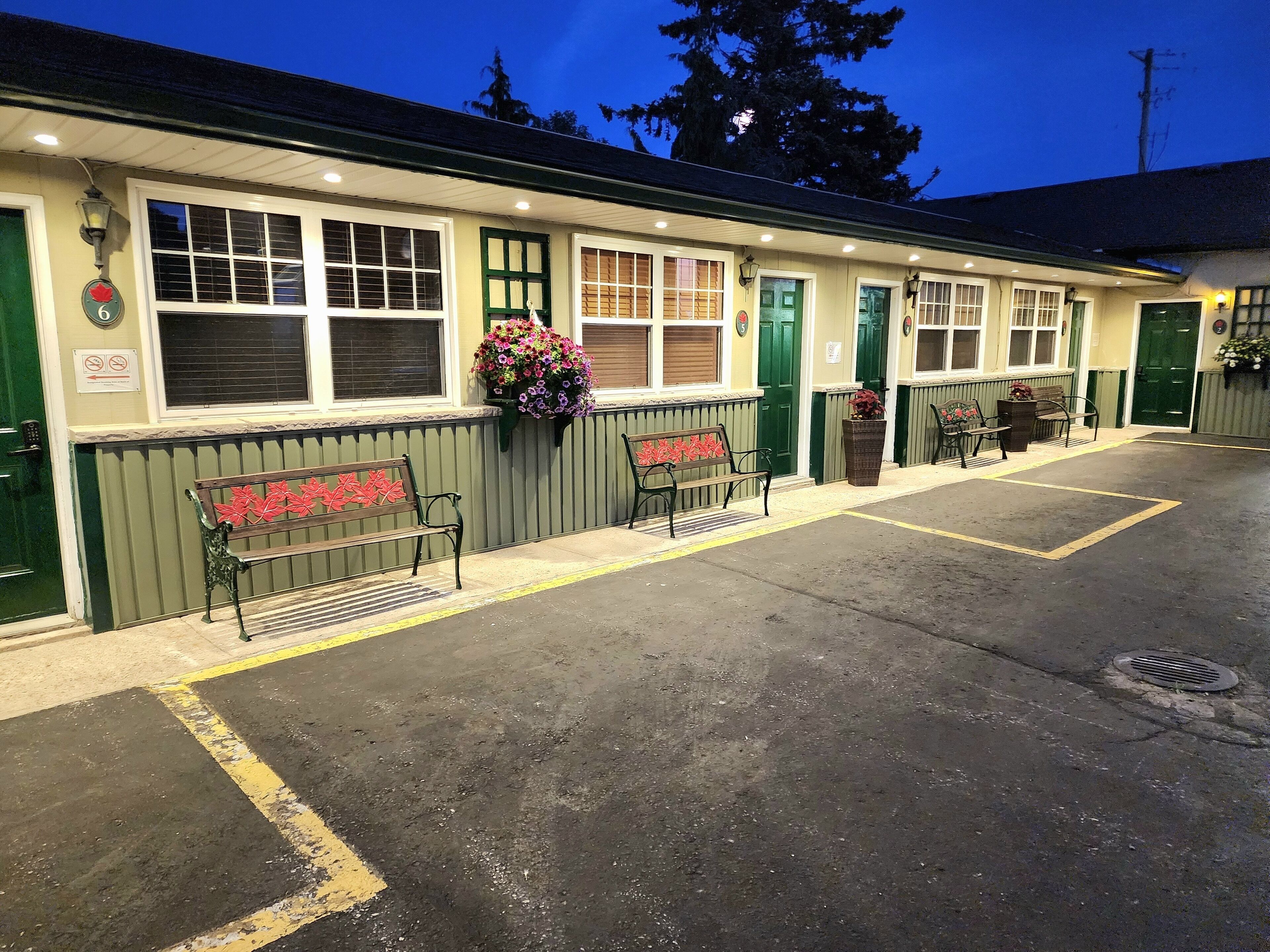 A motel with a row of green-framed windows, a bench with red leaf decorations, and a flower basket on the wall.