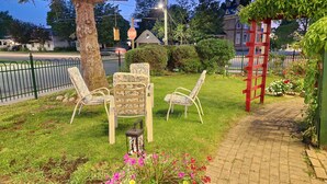 A garden area with a table and two chairs, a red wooden structure, and a paved walkway. - Maple Leaf Motel (Goderich)