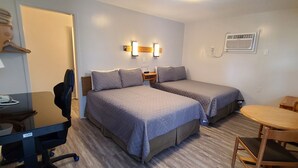 A hotel room with two beds, a desk with a chair, a small table, a TV, and a wall-mounted air conditioner. - Maple Leaf Motel (Goderich)