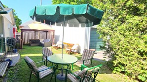 A backyard with a patio area, including a round table and chairs, a bench, and a covered seating area.
