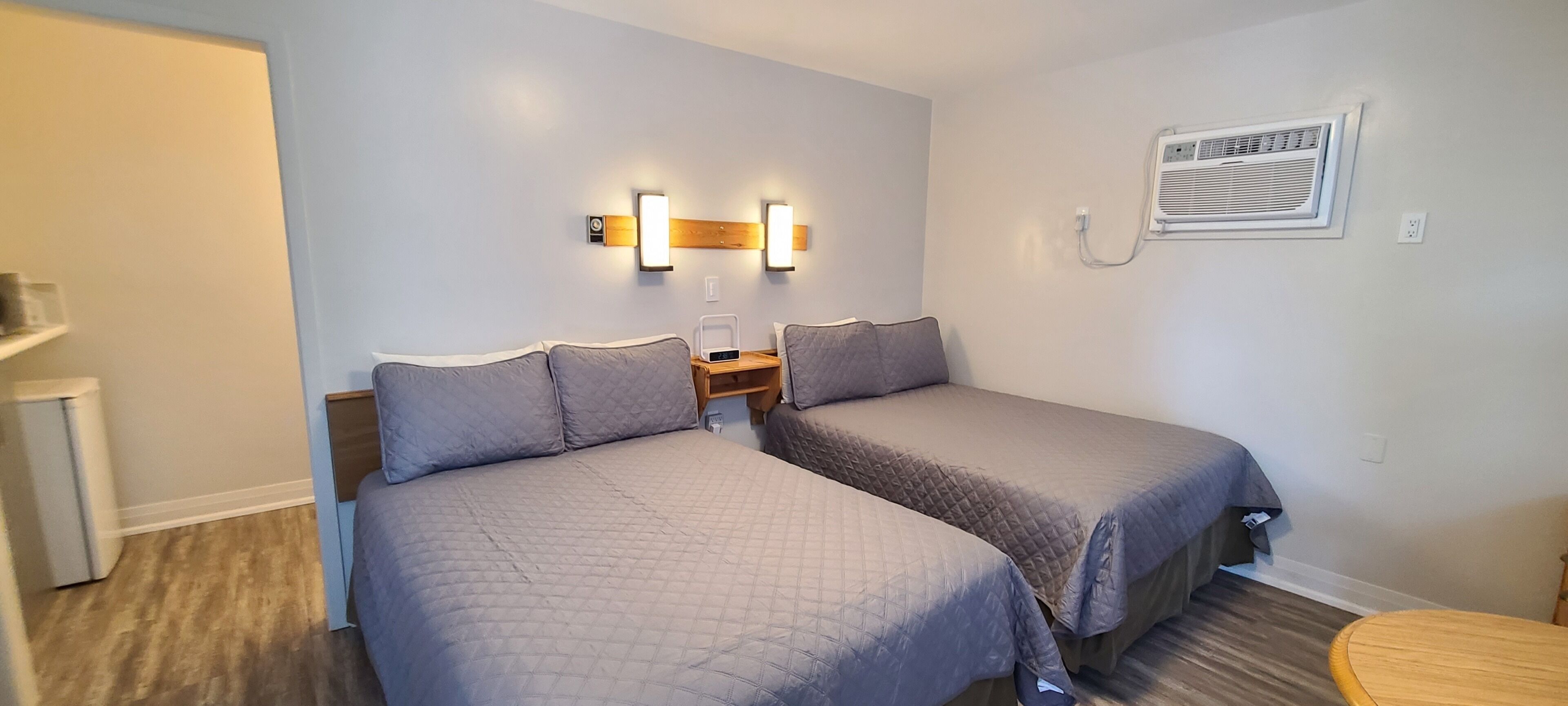A bedroom with two beds, a nightstand, wall-mounted lights, and an air conditioning unit.