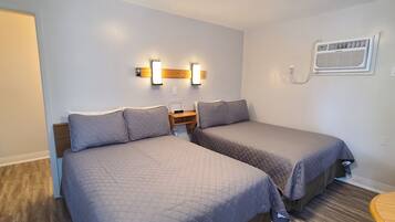 A bedroom with two beds, a nightstand, wall-mounted lights, and an air conditioning unit.