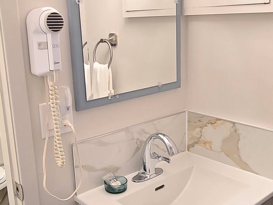 Un baño con un lavabo blanco, un espejo, un perchero para toallas y un secador de pelo.