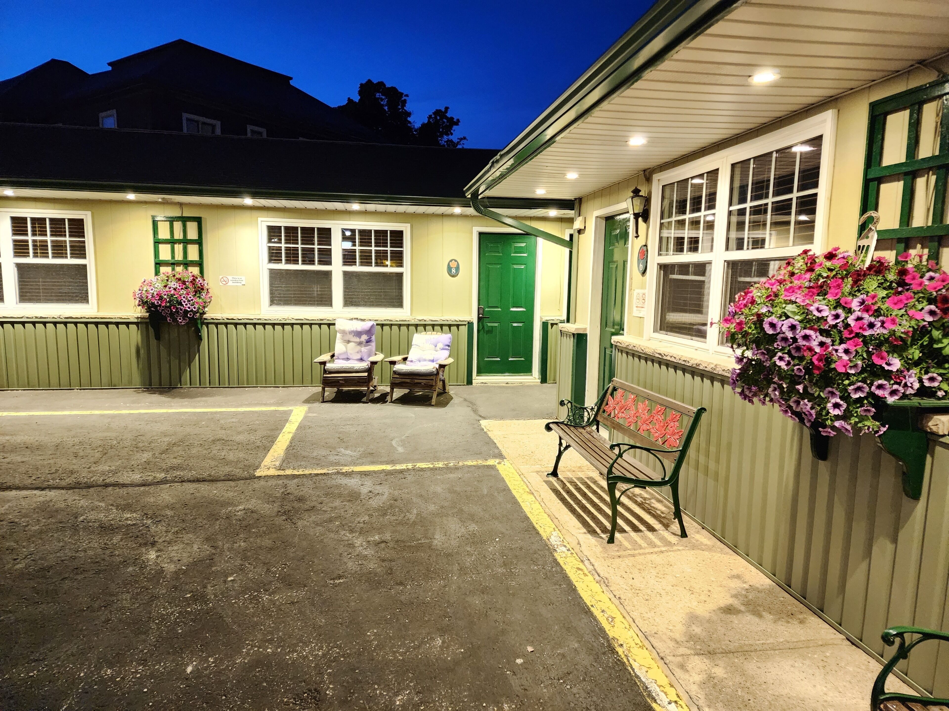 A building with a green door, two armchairs, a bench, and flower baskets.