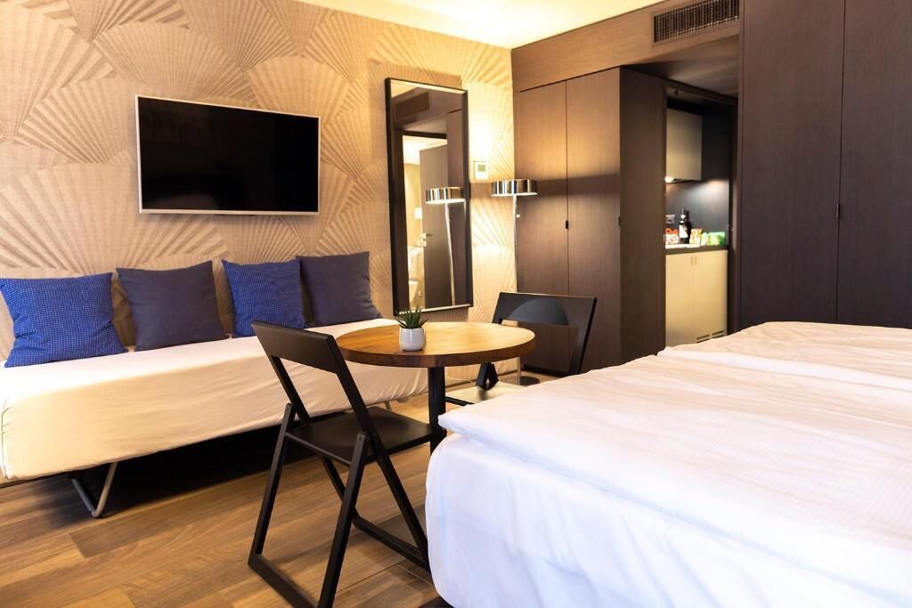 A hotel room with a bed, a sofa, a desk, and a TV.