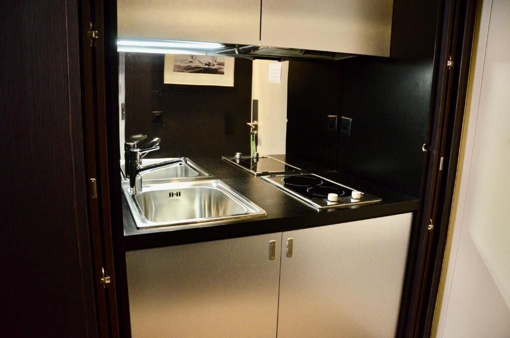 Une cuisine de taille réduite, dotée d’un évier en acier inoxydable, d’une cuisinière à gaz et d’un plan de travail noir.