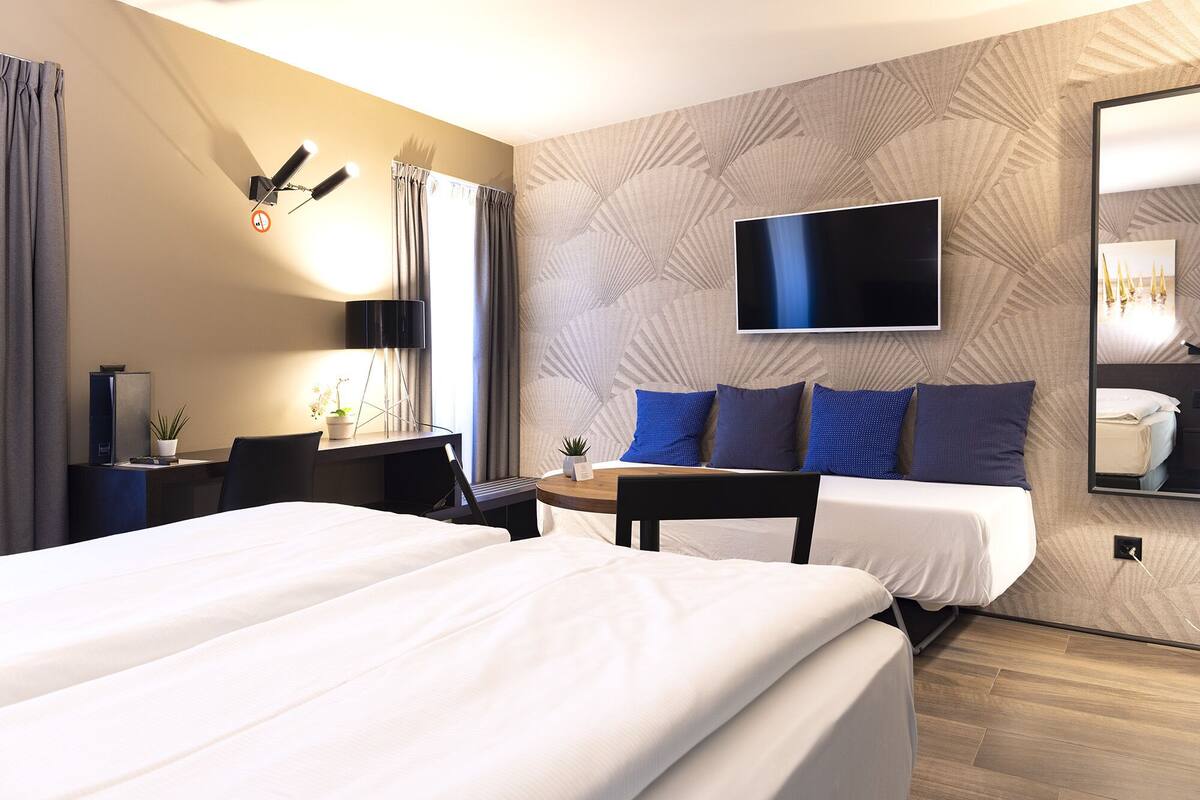 A hotel room with two beds, a desk, a chair, a TV, and a mirror.