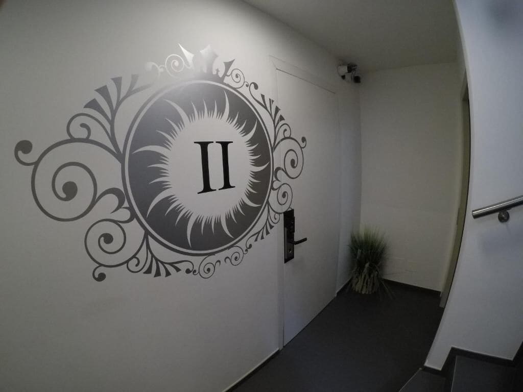 Un pasillo con una pared decorativa que muestra el número 'II' y una planta en la esquina.