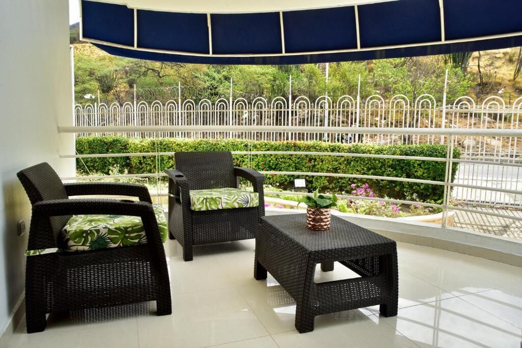 A balcony with wicker furniture, a potted plant, and a view of a garden and fence.