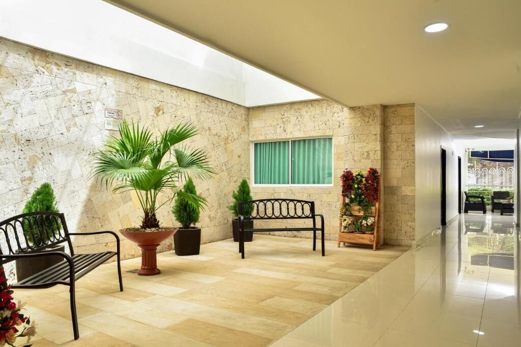 A spacious lobby with a marble floor, a large potted plant, a bench, and a window with green curtains.
