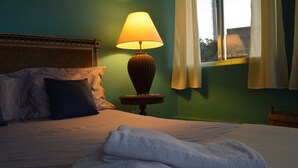 A neatly made bed with a folded towel, a lamp on a bedside table, and a window with curtains. - Banana Leaf Eco Hostel (Rio de Janeiro)
