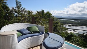 A wicker sofa with cushions and a small round table on an outdoor balcony with a view of a river and bridge. - Banana Leaf Eco Hostel (Rio de Janeiro)