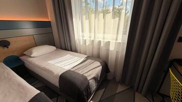 Hotellihuone, jossa on yksi sänky, yöpöytä, tuoli ja ikkuna, jossa on verhot.