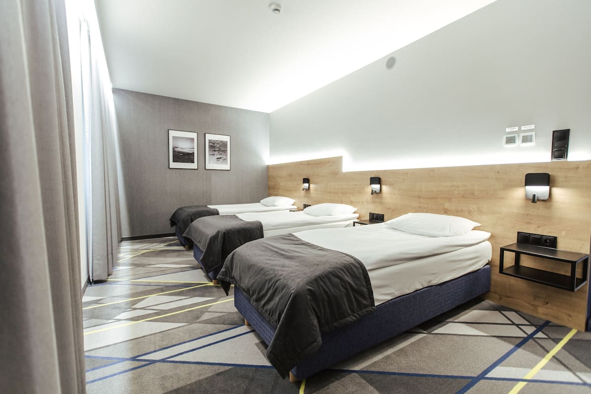 A hotel room with three beds, a wooden headboard, a small bedside table, and a patterned carpet.