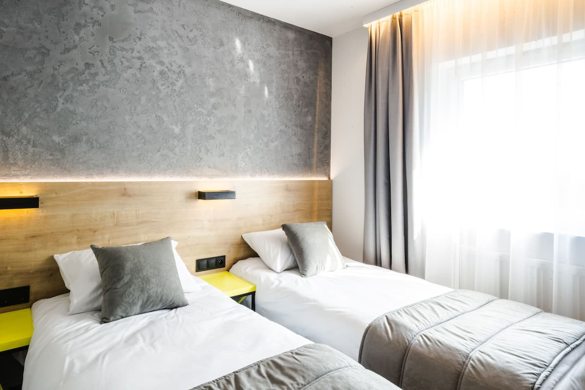 A hotel room with two beds, a wooden headboard, a small table, and a large window with curtains.