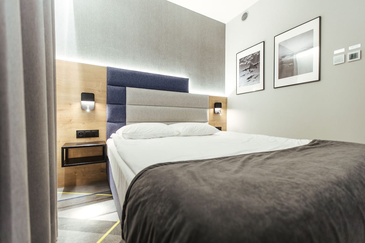 A modern hotel room with a large bed, a wooden headboard, two bedside tables with lamps, and framed pictures on the wall.