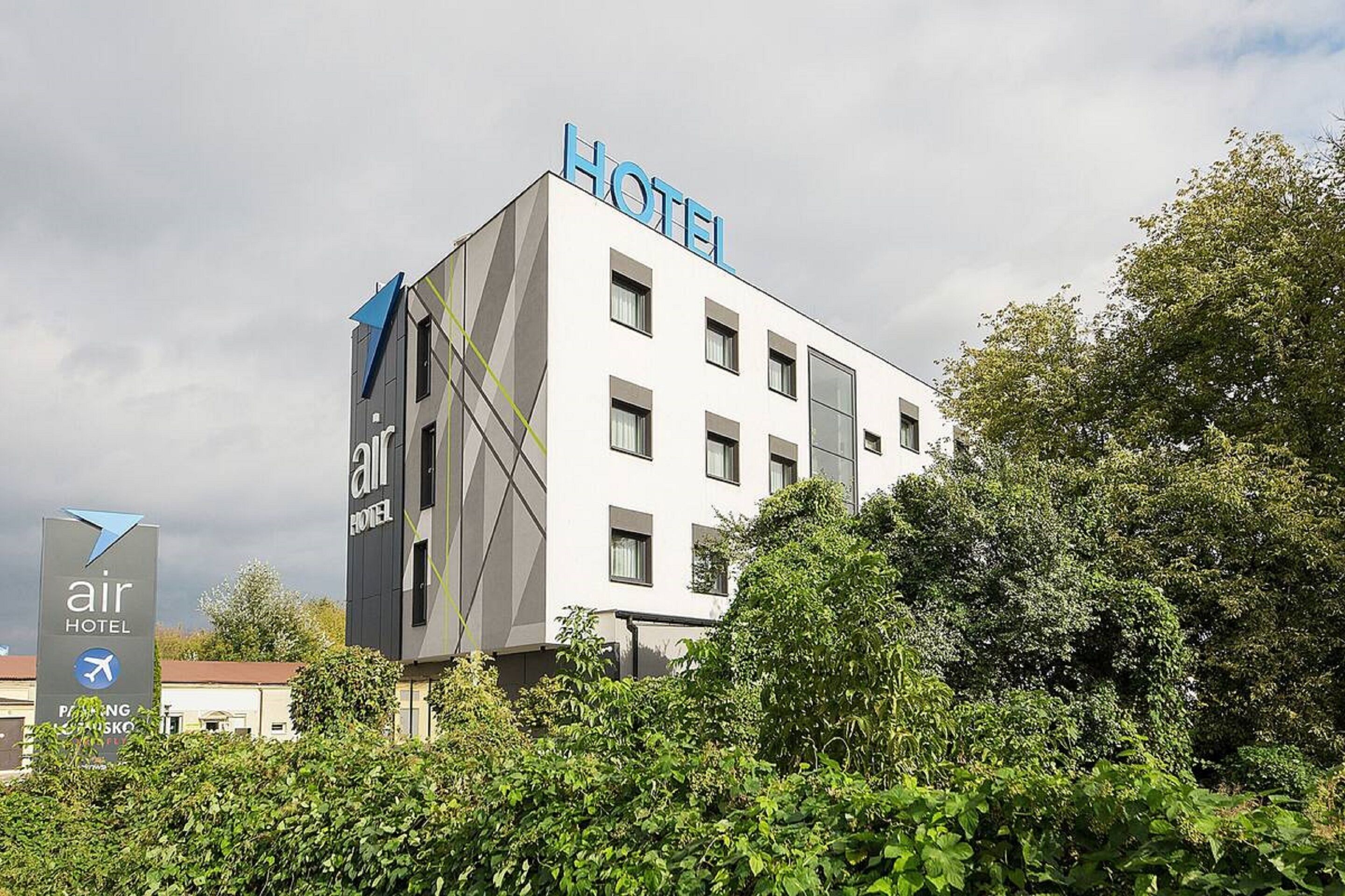 Un moderno edificio de hotel con un llamativo letrero 'HOTEL' en el techo, rodeado de abundante vegetación.