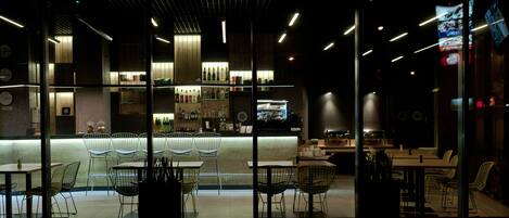 Un restaurante moderno con zona de bar, asientos con sillas de metal y una barra con botellas.
