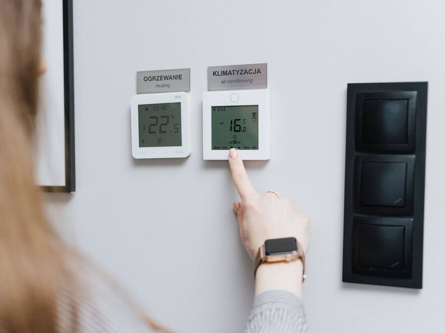 A person adjusting a thermostat with two displays, one labeled "OGRZEWANIE" and the other "KLIMATYZACJA," indicating heating and air conditioning settings.