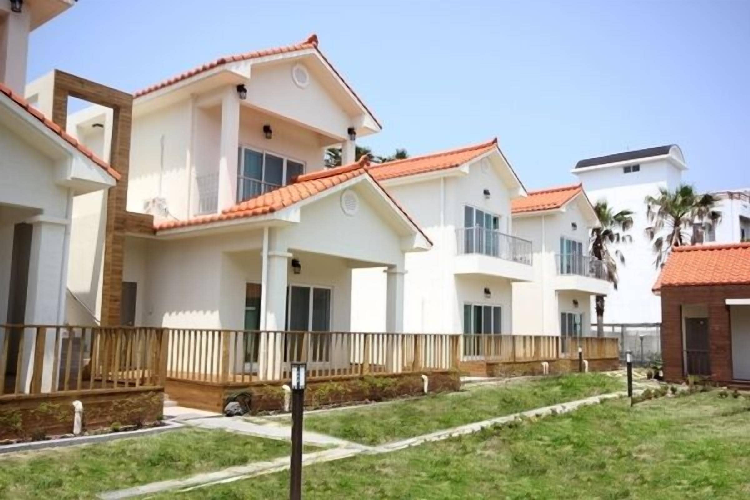 A residential building with a white exterior and red-tiled roofs, featuring balconies and a gated entrance.