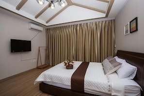 Un dormitorio con cama, televisor de pantalla plana, aire acondicionado y techo con vigas de madera.