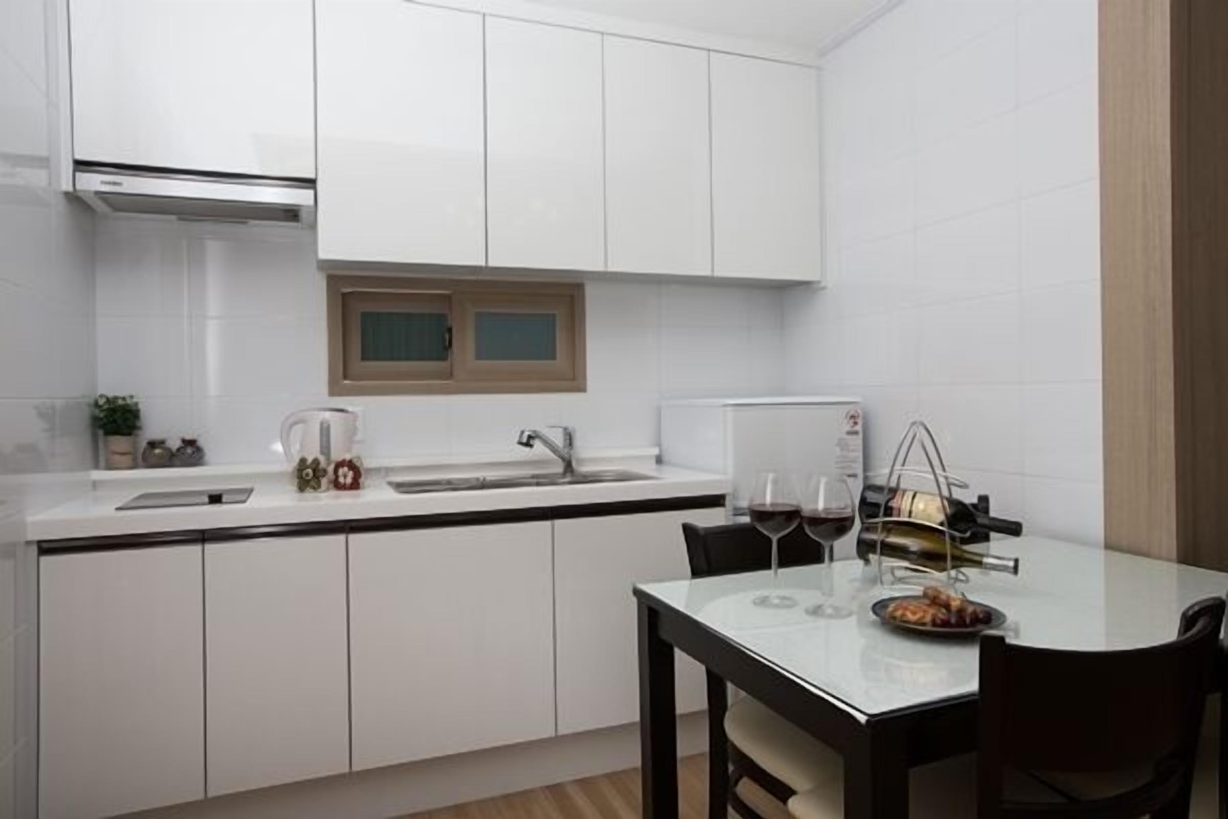 A modern kitchen with white cabinets, a built-in oven, a window, and a dining area with a table and chairs.