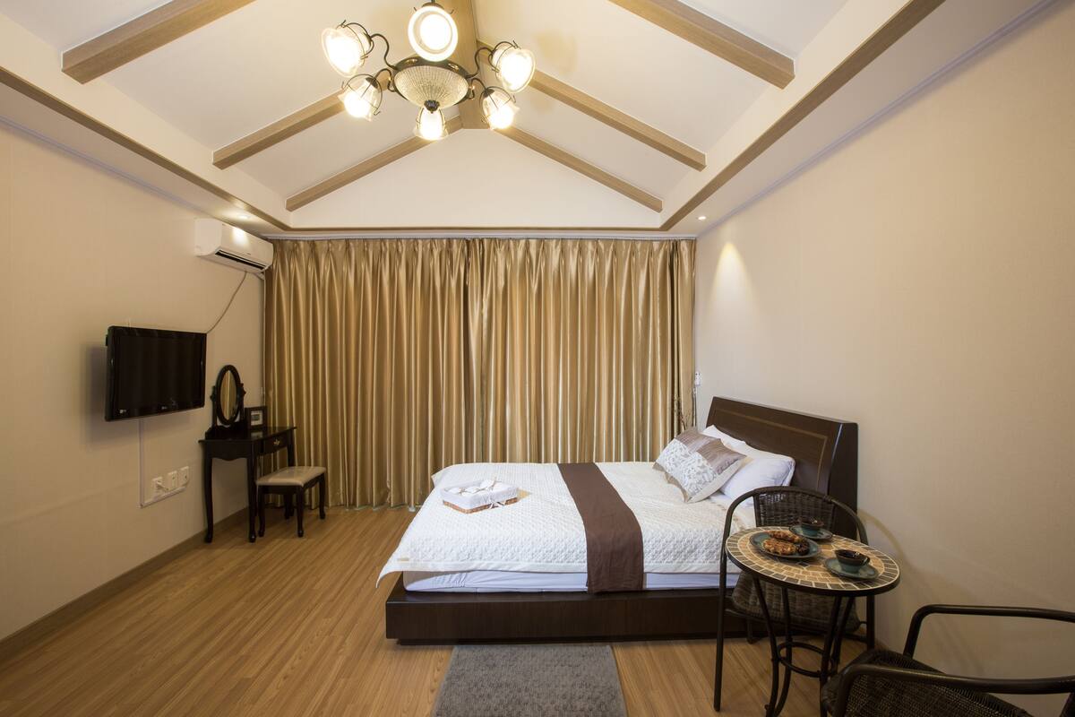 Een slaapkamer met een bed, een kleintje tafeltje met eten, een stoel, een televisie en een gordijn.