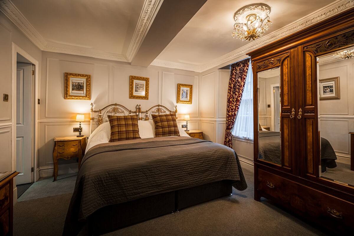 Une chambre à coucher avec un grand lit, deux tables de chevet avec des lampes, un grand miroir et des tableaux encadrés accrochés au mur.