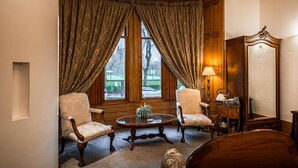 Een kamer met twee fauteuils, een houten bijzettafeltje, een lamp en een spiegel.