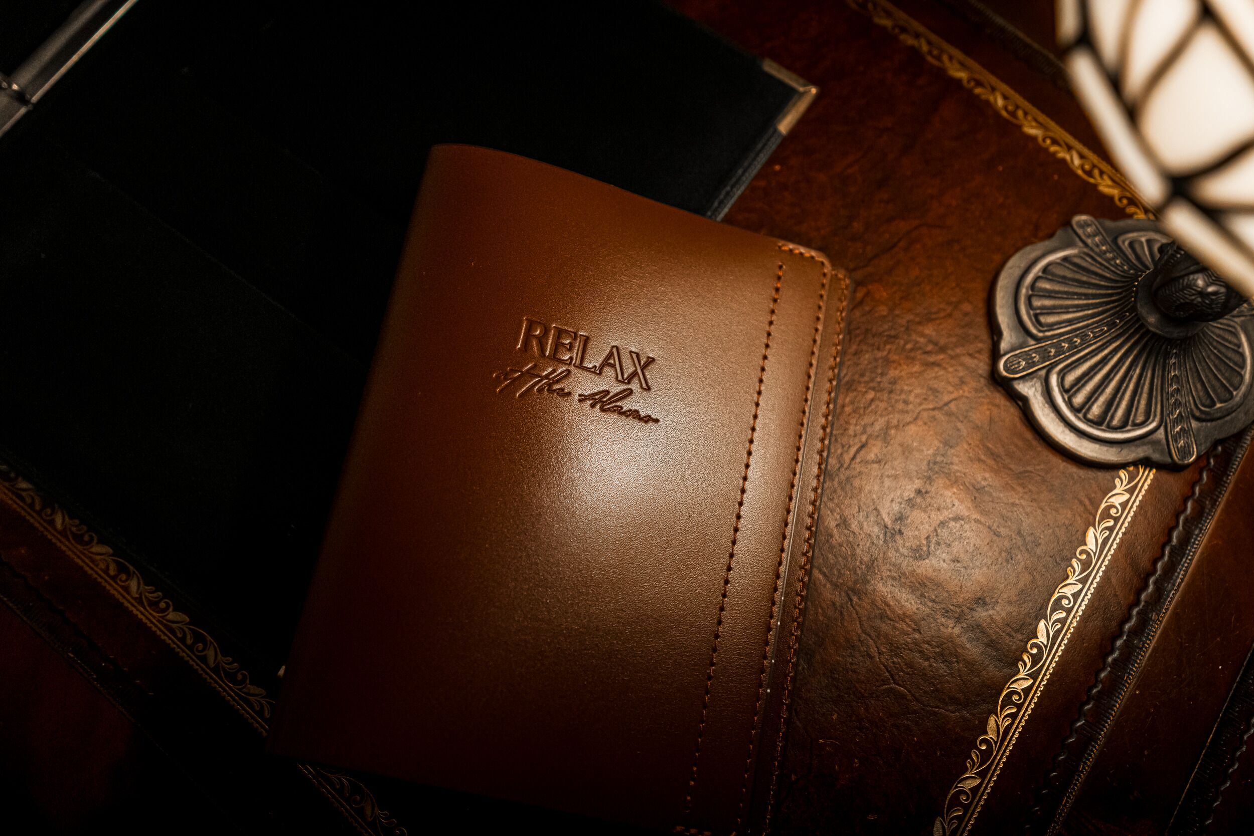 A brown leather-bound book with embossed text, placed on a wooden surface with ornate metalwork.