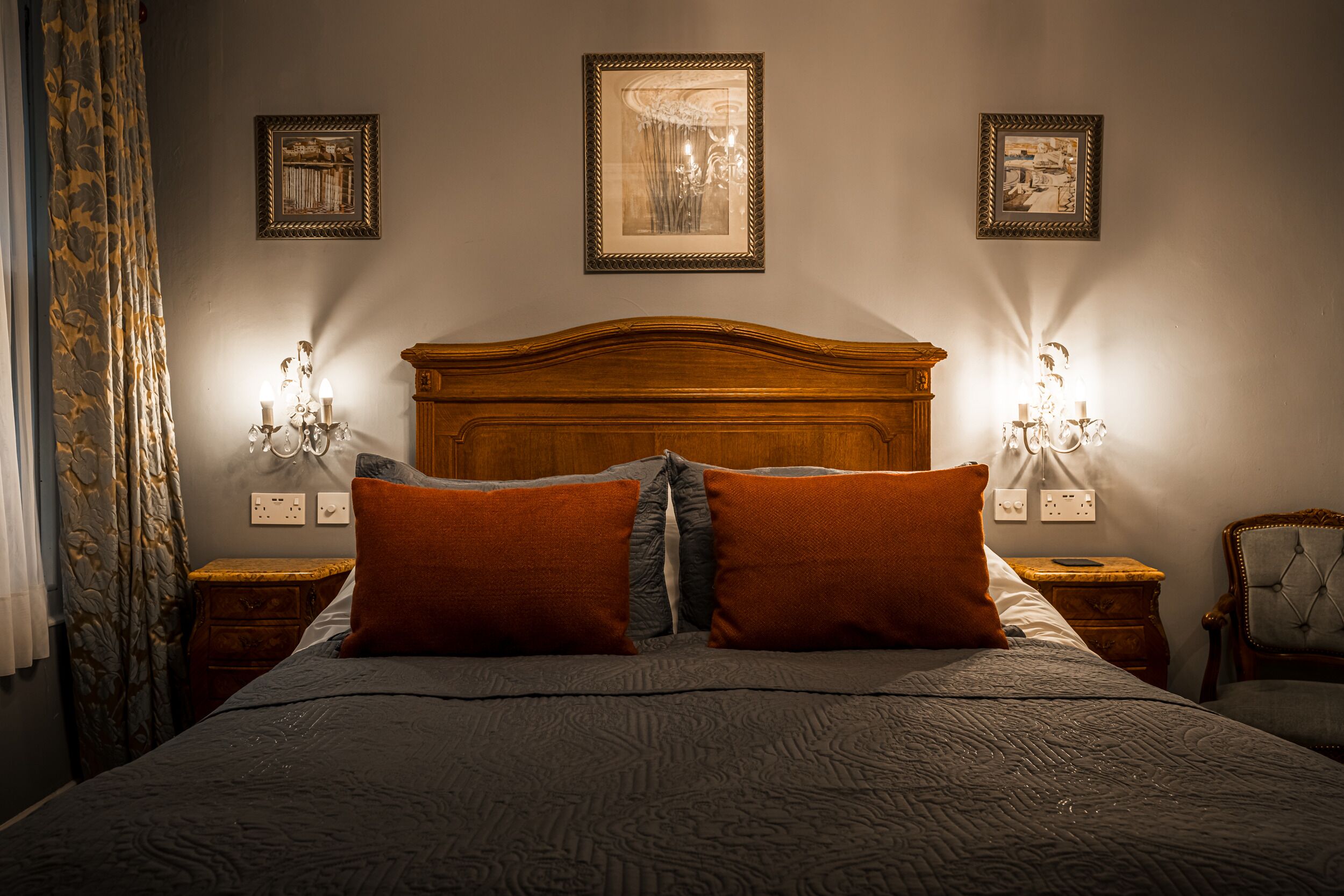 A neatly made bed with a wooden headboard, two wall-mounted lamps, and three framed pictures on the wall.