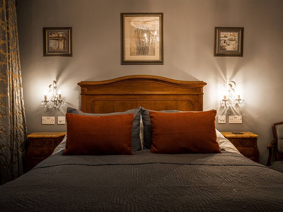 A neatly made bed with a wooden headboard, two wall-mounted lamps, and three framed pictures on the wall.