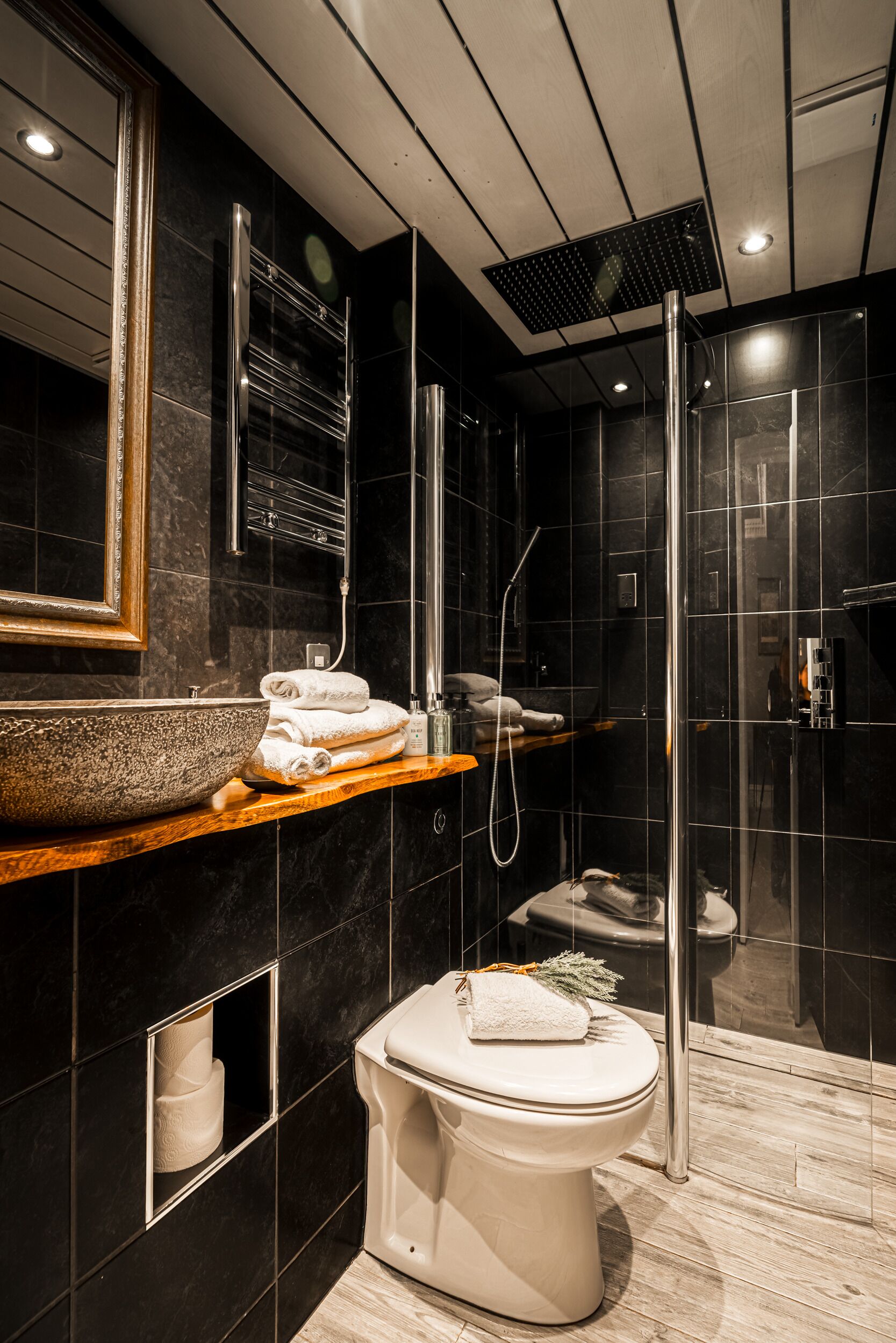 A modern bathroom with a large mirror, a vessel sink, a toilet, and a glass-enclosed shower.