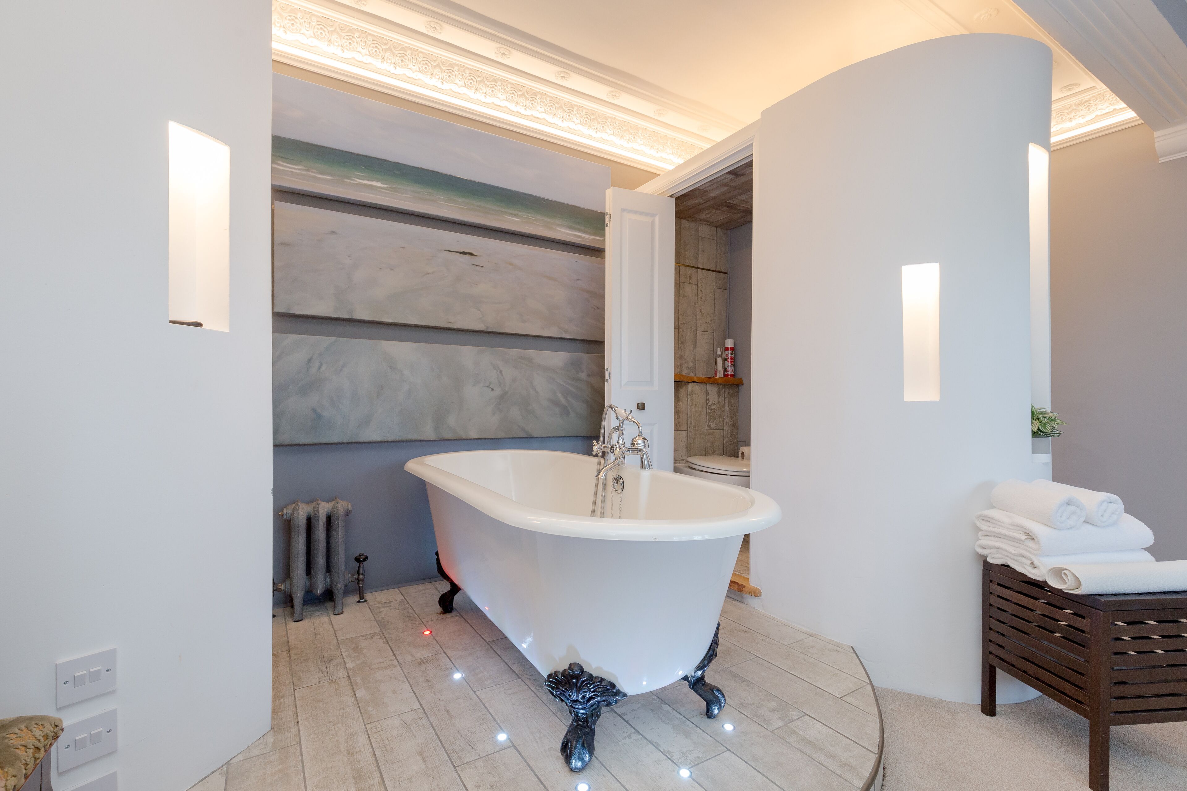 A modern bathroom with a freestanding bathtub, a radiator, and a wooden bench with towels.