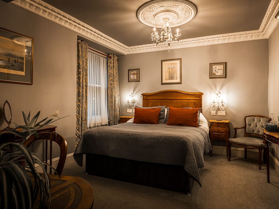 Een smaakvol ingerichte slaapkamer met een groot bed, twee nachtkastjes, een stoel en een bureau.