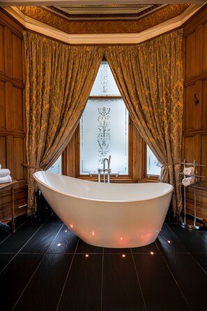 A large freestanding bathtub in a room with dark wooden paneling and a large window with curtains. - Alamo Guest House (Glasgow)