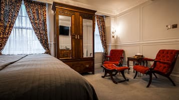Quarto de hotel com uma cama grande, um guarda-roupa de madeira, duas poltronas vermelhas e uma mesinha.