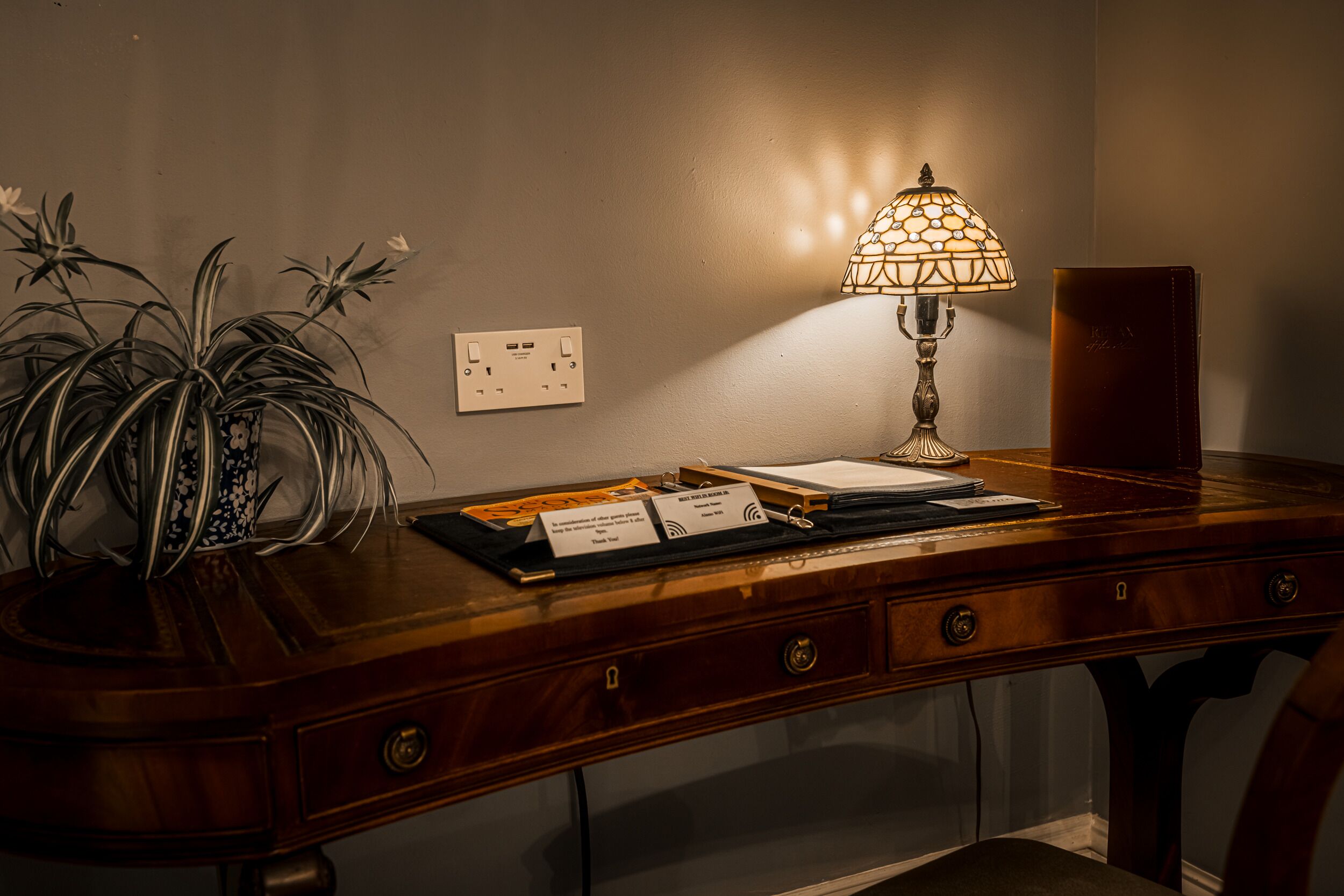 A wooden desk with a lamp, papers, and a nameplate.