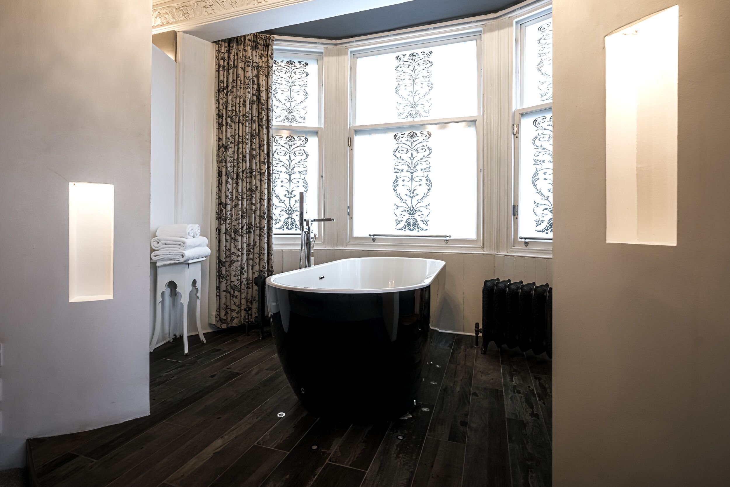 Een moderne badkamer met een vrijstaand bad, een radiator en een raam met decoratieve gordijnen.