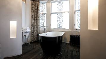 Een moderne badkamer met een vrijstaand bad, een radiator en een raam met decoratieve gordijnen.