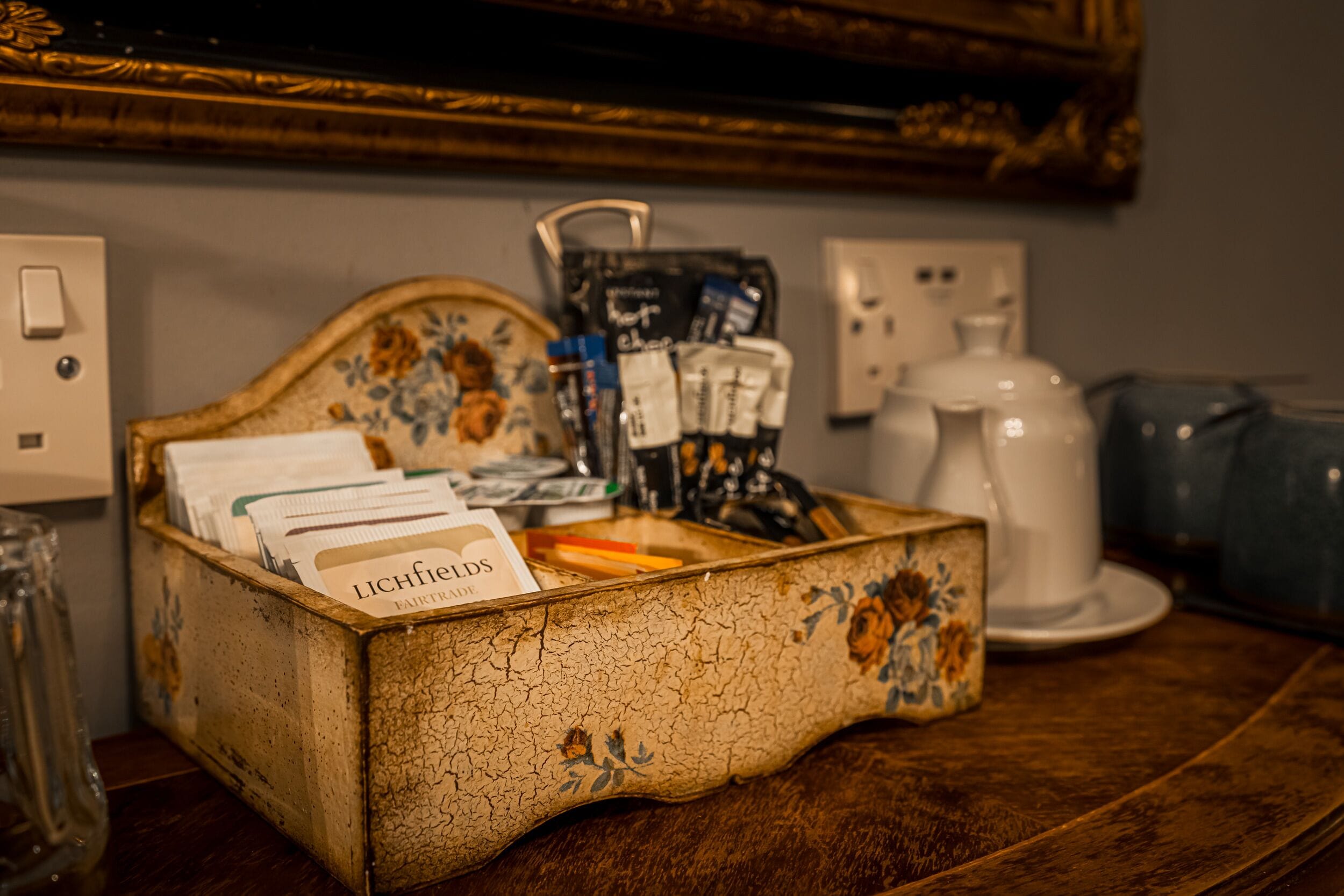 Caixa de madeira com design floral que contém vários itens, incluindo cartões, uma cafeteira e um pequeno recipiente.