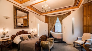 Een ruime slaapkamer met een groot bed, een zithoek met een fauteuil, een kaptafel en een badkuip.