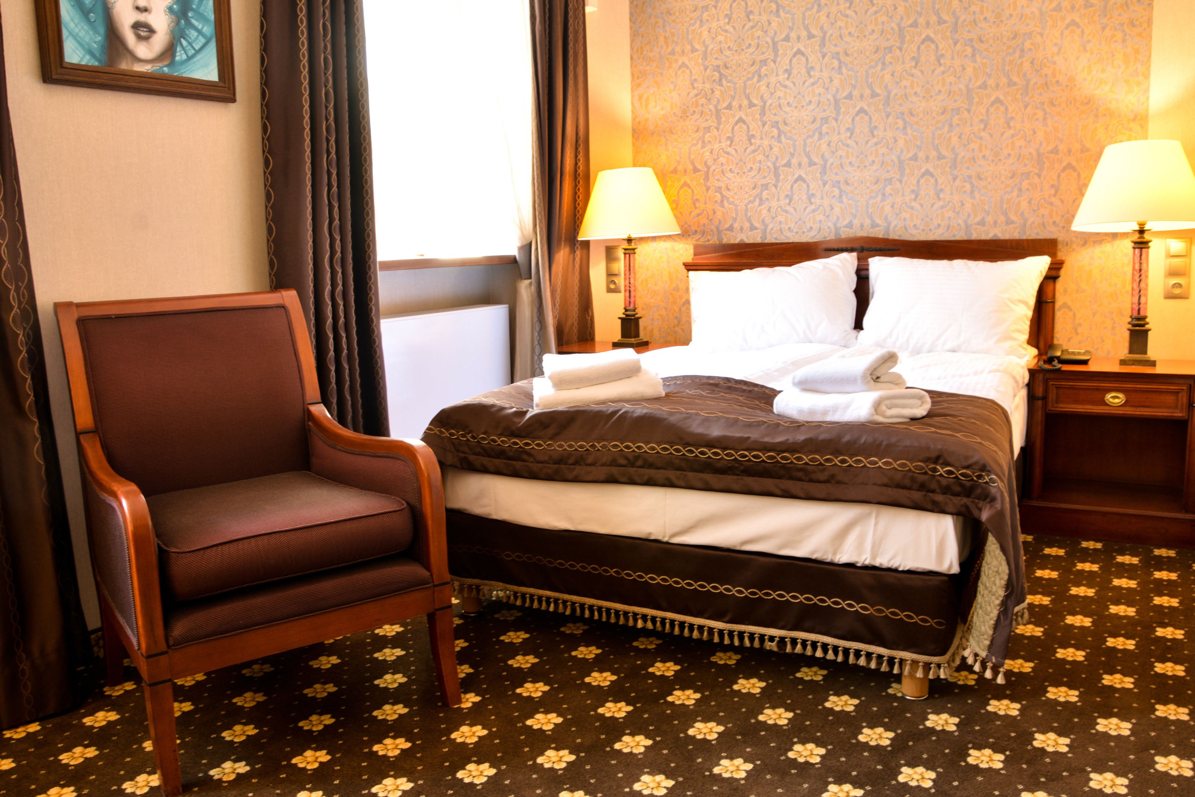 A hotel room with a bed, two bedside lamps, a chair, and a floral-patterned carpet.
