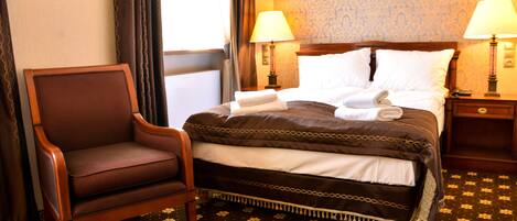 A hotel room with a bed, two bedside lamps, a chair, and a floral-patterned carpet.