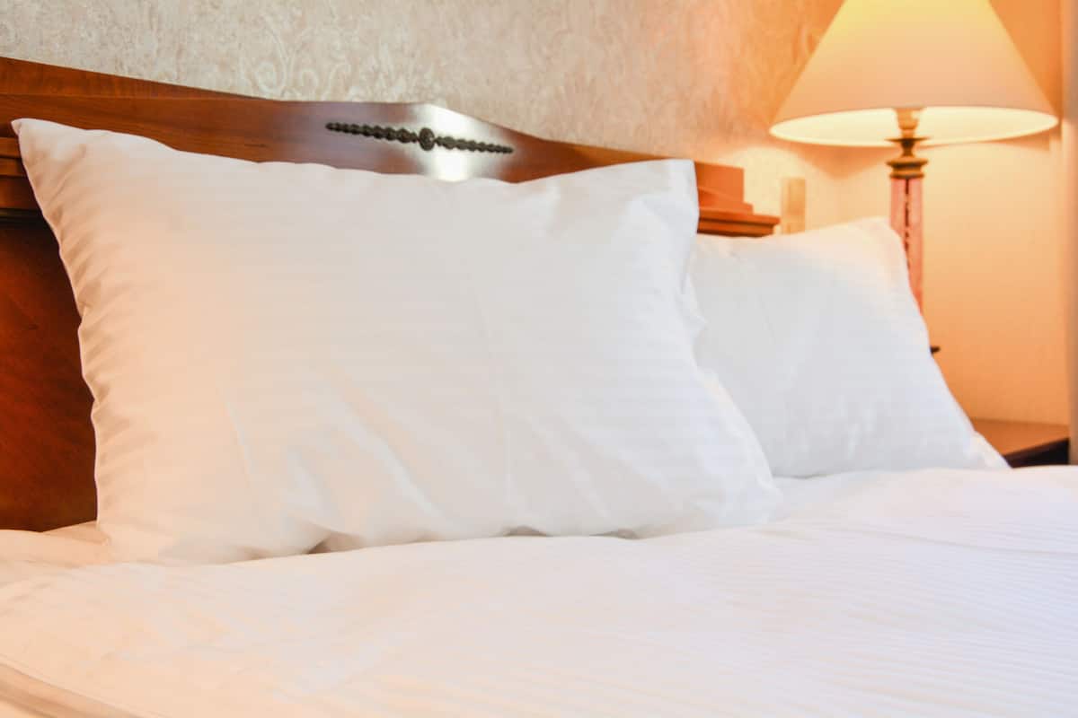 A neatly made bed with white linens and a wooden headboard.
