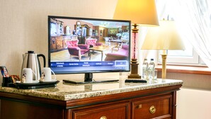 A hotel room with a television displaying a room layout, a coffee maker, a lamp, and a window with curtains. - Komoda Club Residence (Kalisz)